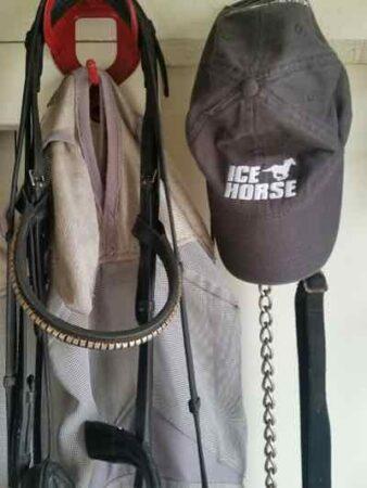 bridle fly mask and hat all hanging in a tack room